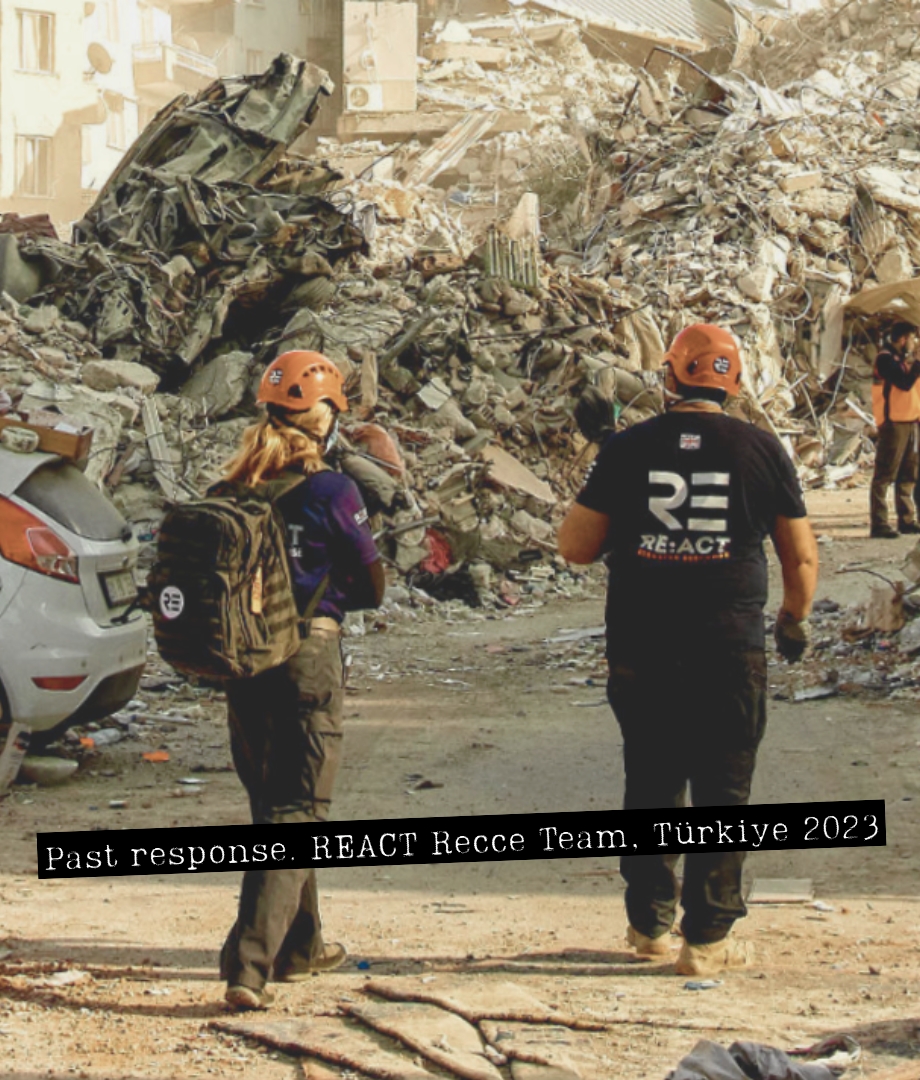 Two REACT responders wearing helmets walk through a street of collapsed buildings after the 2023 Türkiye earthquakes. This is a past response image, used to illustrate the capability your donation supports as REACT monitors the Afghanistan earthquake.